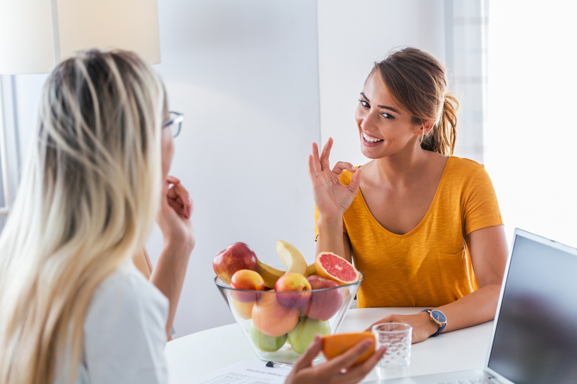 Professional Nutritionist Meeting a Patient in the Office. Young Smiling Female Nutritionist in the Consultation Room. Nutritionist Desk With Healthy Fruit and Measuring Tape.