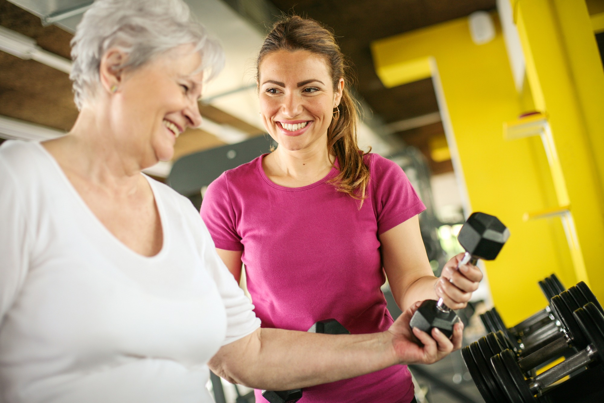Personal Trainer Working Exercise With Senior Woman in the Gym. Woman Picking Weight. Workout in Gym.